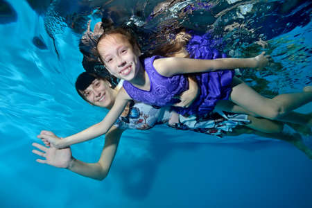 Happy family: mother and daughter hugging,floating underwater, holding hands. They smile and look at the camera. Underwater photography. Portrait. Horizontal orientation.の写真素材