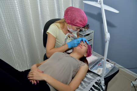 The cosmetologist performs the procedure of microblading eyebrows in the beauty salon with the help of a cosmetic tool. Portrait. Close up. Horizontal view.の写真素材