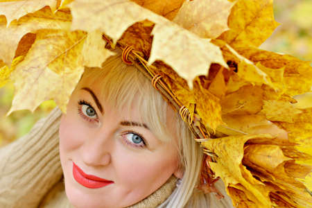 Cute big blonde in a wreath of yellow autumn leaves in the forest on a yellow background, looking up in the frame. Size Plus xxl female. Portrait. Close up.の写真素材