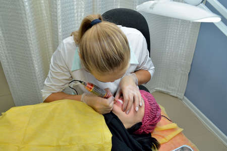 A beautiful girl-cosmetologist in a beauty salon does the procedure of permanent makeup of the lips. The view from the top. The concept of beauty. Horizontal orientation of the image.の写真素材