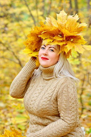 A large beautiful blonde girl surrounded by autumn leaves, sitting in the forest on a yellow background in a gentle jumper. The view from the top. Close up. Plus size xxl female. Vertical view.の写真素材