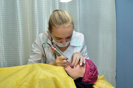 In the beauty salon, a master beautician, a blonde makes permanent makeup lips European girl. Concept. Close up. Horizontal orientation of the image.の写真素材