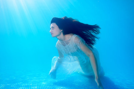 Unusual mermaid bride swims underwater in the pool with long flowing hair in a white dress on the...