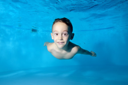 Portrait of a beautiful athletic boy underwater in the pool. Fun dives under the water. Swimming classes. Bodily exercises. Healthy lifestyleの写真素材