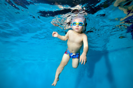 Portrait of a boy in a Santa hat and glasses in a pool underwater. The kid learns to have fun diving under water. Swimming lessons with a child. Healthy lifestyle. Horizontal orientationの写真素材