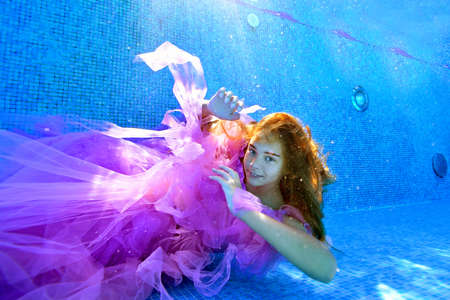 Cute girl posing in a beautiful dress at the bottom of an outdoor pool. She looks at the camera and smiles. Portrait. Wide angle. Horizontal orientation.の写真素材