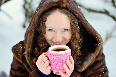 Portrait of a young beautiful girl with a Cup of tea on a winter day in a snow-covered forest. I want to keep warm. Smile. Heat. Horizontal orientation.の写真素材