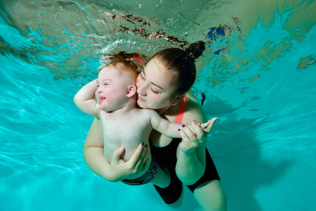 A happy mother hugs her baby with Down syndrome tightly and swims with him underwater in a childrens...
