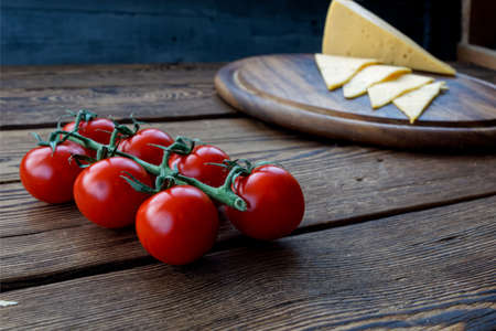 slice cheese and cherry tomatos on wooden cutting boardの写真素材