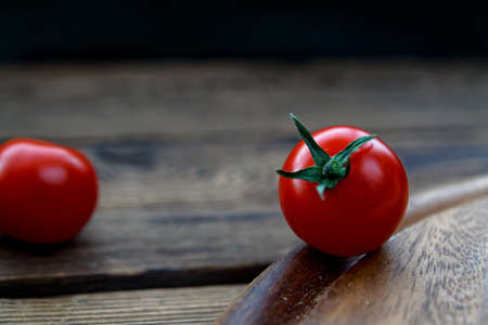 two cherry tomatoes on wooden cutting board against a dark backgroundの写真素材