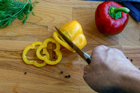 hand cutting yellow bell pepper on a wooden cutting boardの写真素材