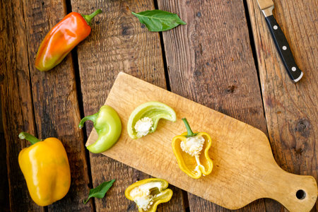 multi-colored bell pepper, whole and sliced, laid out on a cutting board on a background of old wooden boardsの写真素材