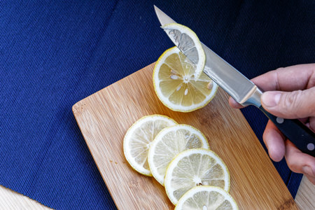 slicing a lemon with a kitchen knife on a cutting board. lemon slices on a wooden board