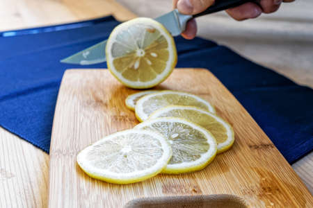 slicing a lemon with a kitchen knife on a cutting board. lemon slices on a wooden boardの写真素材