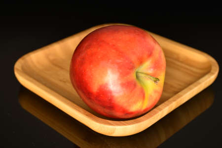 One red juicy apple on a bamboo tray on a black background.の写真素材