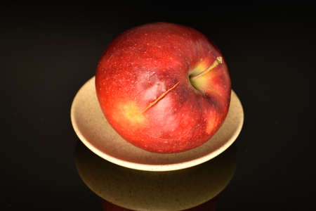 One red ripe apple, on a saucer, on a black background.の写真素材
