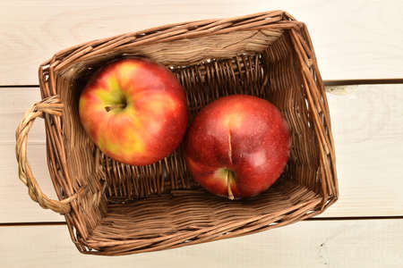 Two red juicy fresh apple in a basket on a painted wooden table.の写真素材