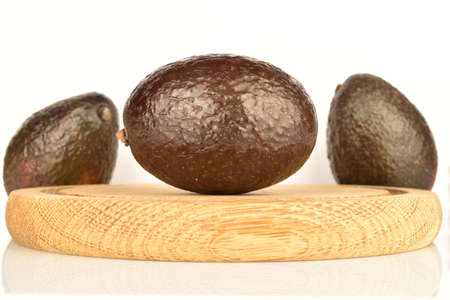 Three dark green, ripe fragrant tasty avocados, lies on a brown wooden round stand. The background is white.の写真素材