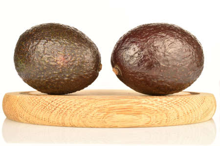 Two dark green, ripe fragrant tasty avocados, lies on a brown wooden round stand. The background is white.の写真素材