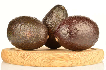 Three dark green, ripe fragrant tasty avocados, lies on a brown wooden round stand. The background is white.の写真素材