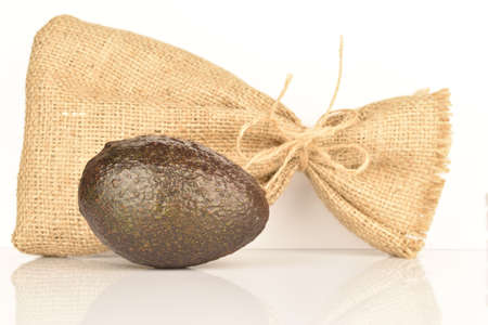 One whole, dark green, ripe aromatic delicious avocado, lie next to a jute bag. The background is white.の写真素材