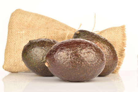 Three whole, dark green, ripe aromatic delicious avocados lie next to the jute bag. The background is white.の写真素材