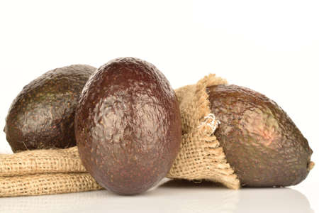Three whole, dark green, ripe aromatic delicious avocados lie next to the jute bag. The background is white.の写真素材