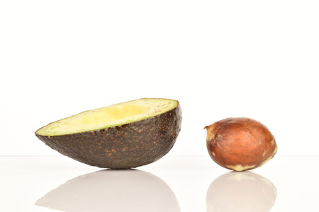 One half, dark green, ripe aromatic tasty avocado, next to it lies one whole brown stone from the...