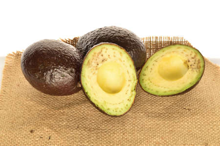 Two whole and two halves, dark green, ripe aromatic delicious avocados, lie on jute fabric. The background is white.の写真素材