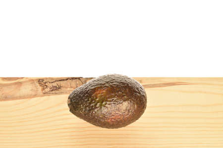 One whole dark green rounded ripe tasty nutritious avocado lies on a wooden tabletop.の写真素材