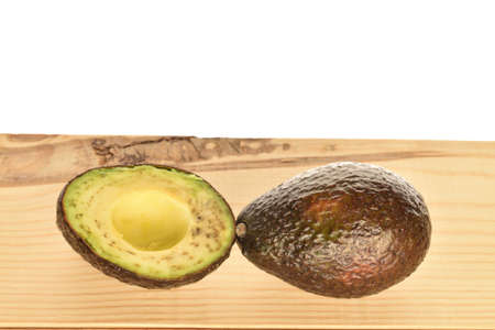 One whole and one half dark green ripe tasty nutritious avocado lie on a wooden tabletop.の写真素材