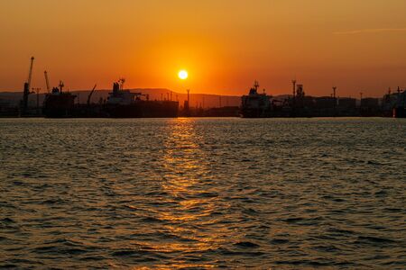 The silhouette of the port of Novorossiysk at sunset and the reflection of sunset in the waves of Black seaの写真素材