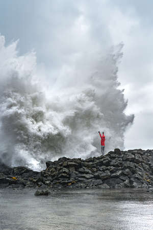 A man in a red jacket standing in front of a huge waveの写真素材