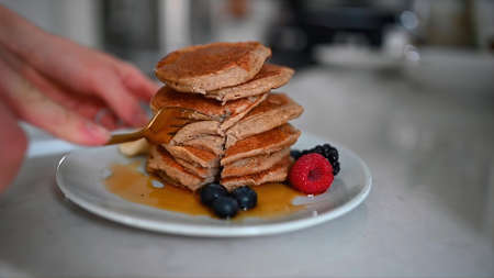 Pancakes sprinkled with honey and raspberries on a plate are cut with a fork. Eat.の写真素材