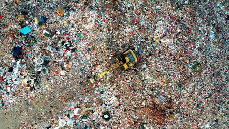 Tractor on a mountain of garbage. Tractor with a bucket on the garbage. Photo taken from above. Below the tents of the homeless. Save the planet.の写真素材