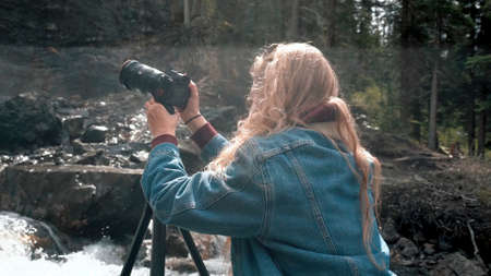 Girl photographer. Back view. Traveler photographing scenic view in forest. One caucasian woman shooting nice magic look. Girl take photo video on dslr mirrorless camera.の写真素材