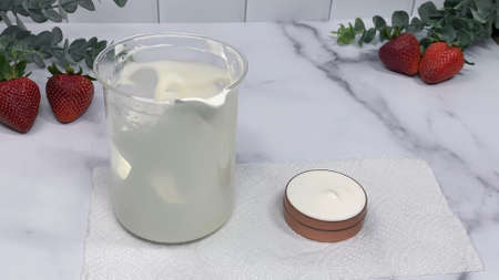DIY beauty cream, white cream in a jar and measuring cup, strawberries in the backgroundの写真素材