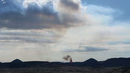 Eruption of a volcano against the background of a blue sky with clouds. Lava splash. Smoke from the volcano.の写真素材