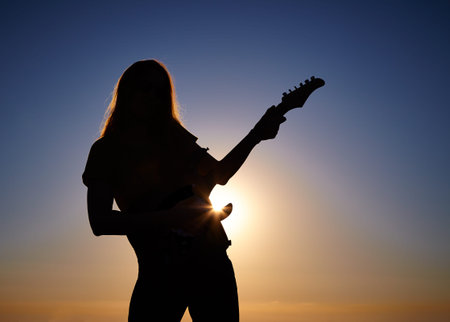 Bending body of female musician keeping the guitar on the rising sun backgroundの写真素材