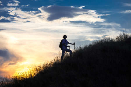 Mountain hiker in front of sunset Silhouette of person with arms outstretched staying on the steep slope with bright sunset on the backgroundの写真素材