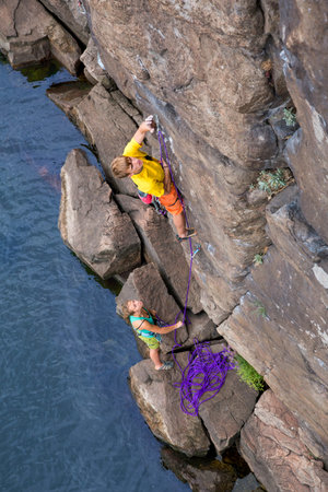 Climbing partners make ascent on to the rock wall Two climbers  male and female  climb rocky wall. Young male climber is leading female teenager is belaying himの写真素材