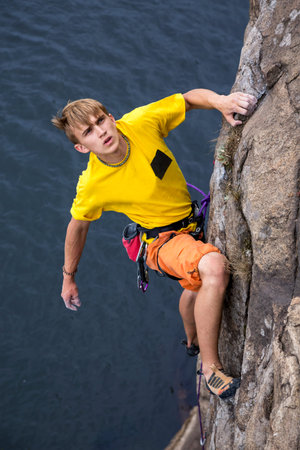 Young male rock climber hanging over the water making his next difficult move. Serious manful faceの写真素材