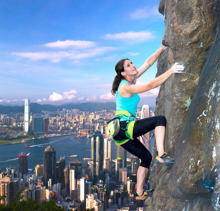 Female rock climber over the city skyline Beautiful female extreme climber ascents the rocky wall over the modern cityの写真素材