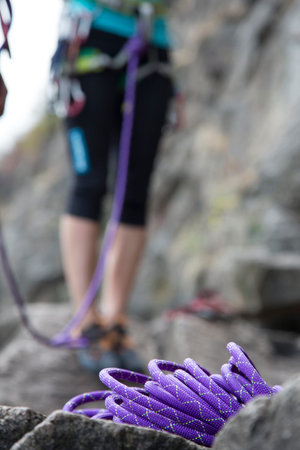 Purple climbing rope and legs of climber New and clean purple sport climbing rope on the stone...