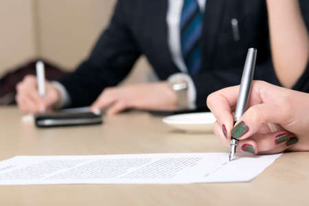 Female businessperson signs contract Close up of female hand signing formal paper on the office table. The business counterpart on the backgroundの写真素材