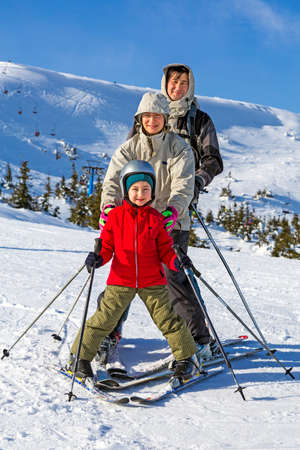 Family of three people learns skiing together Mixed race family stays on the snow slope with the skis attached. Happy, smiling, joyfulの写真素材