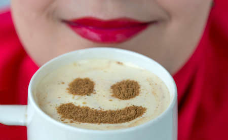 Coffee mug with smiley shape on the froth Close-up image of cappuccino surface with smiley shape and bright red female lipsの写真素材