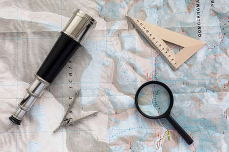 Desk of explorer Top view of desk covered with the topographic map with typical items navigator: sea telescope, navigational triangle, magnifier and compassの写真素材