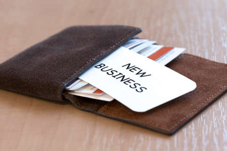 New business Conceptual composition with leather business-card folder, stack of colourful business cards and white business card with phrase New Business on foregroundの写真素材
