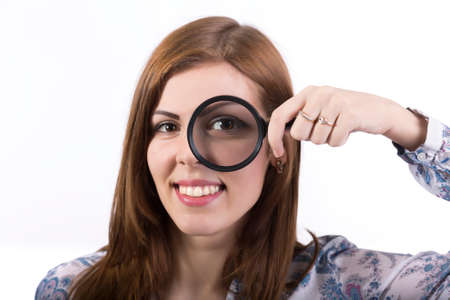 Female face looking through magnifier Portrait of young smiling female with an eye looking throw magnifying glassの写真素材